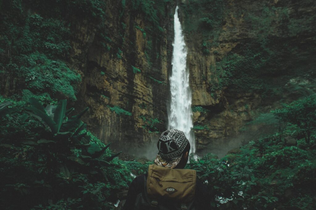 Man in forest with large waterfall in the back ground, seeking self exploration