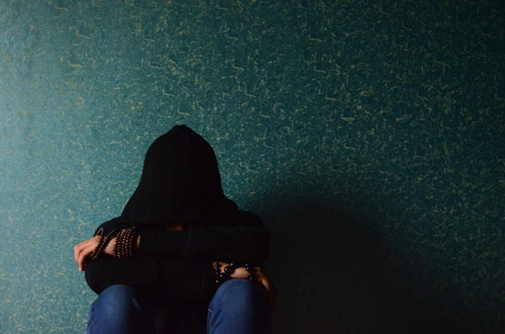 Someone crouch down on the floor and a black hood, depressed in front of an emerald green wall