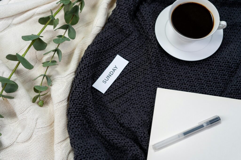 Cup of coffee on a coy blanket lying on a table with the word Sunday cut out on a piece fo paper