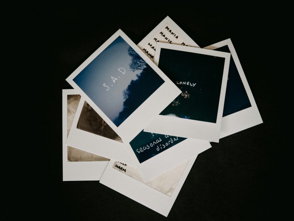 A scattered stack of Polaroid photos with words like “S.A.D” and “lonely,” symbolizing emotional meaning, mental health, and the importance of emotional intelligence.