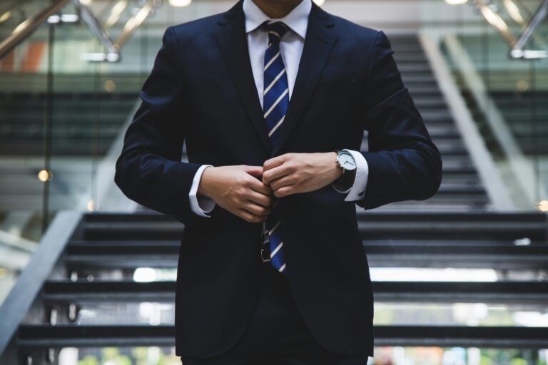 Professional business executive in formal suit adjusting jacket in corporate office building, representing outward appearance of leadership competence while facing internal identity constraints and growth plateaus.