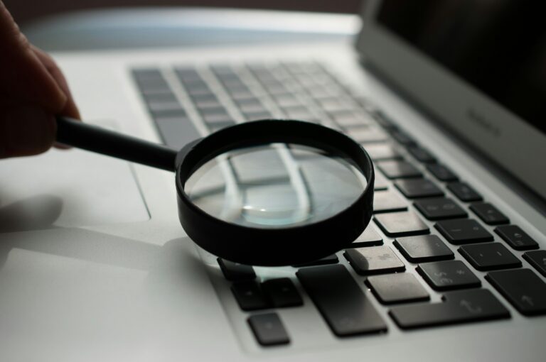 Close-up of magnifying glass over keyboard representing the deeper analysis required to uncover identity constraints preventing leadership teams from evolving and scaling effectively.